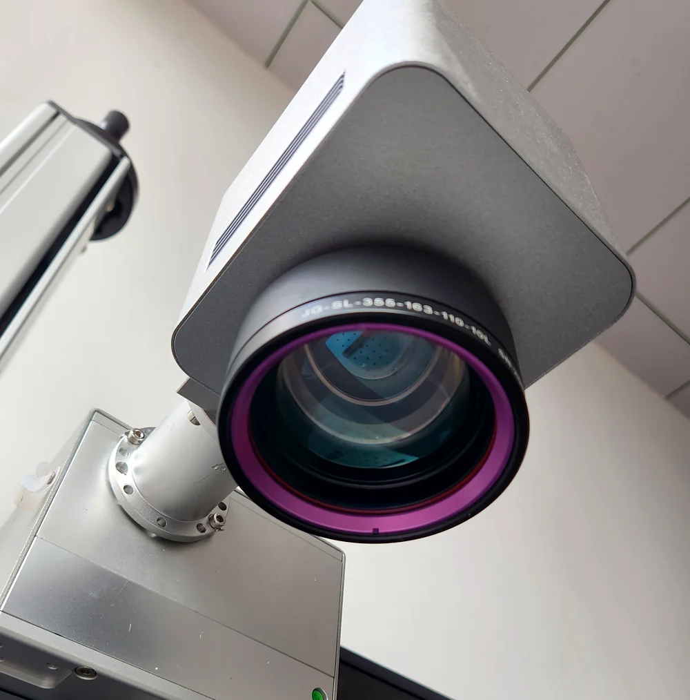 Close-up of the f-theta scan lens on a Laserhi UV marking head, barrel marked 355 nm with 163 mm focal length